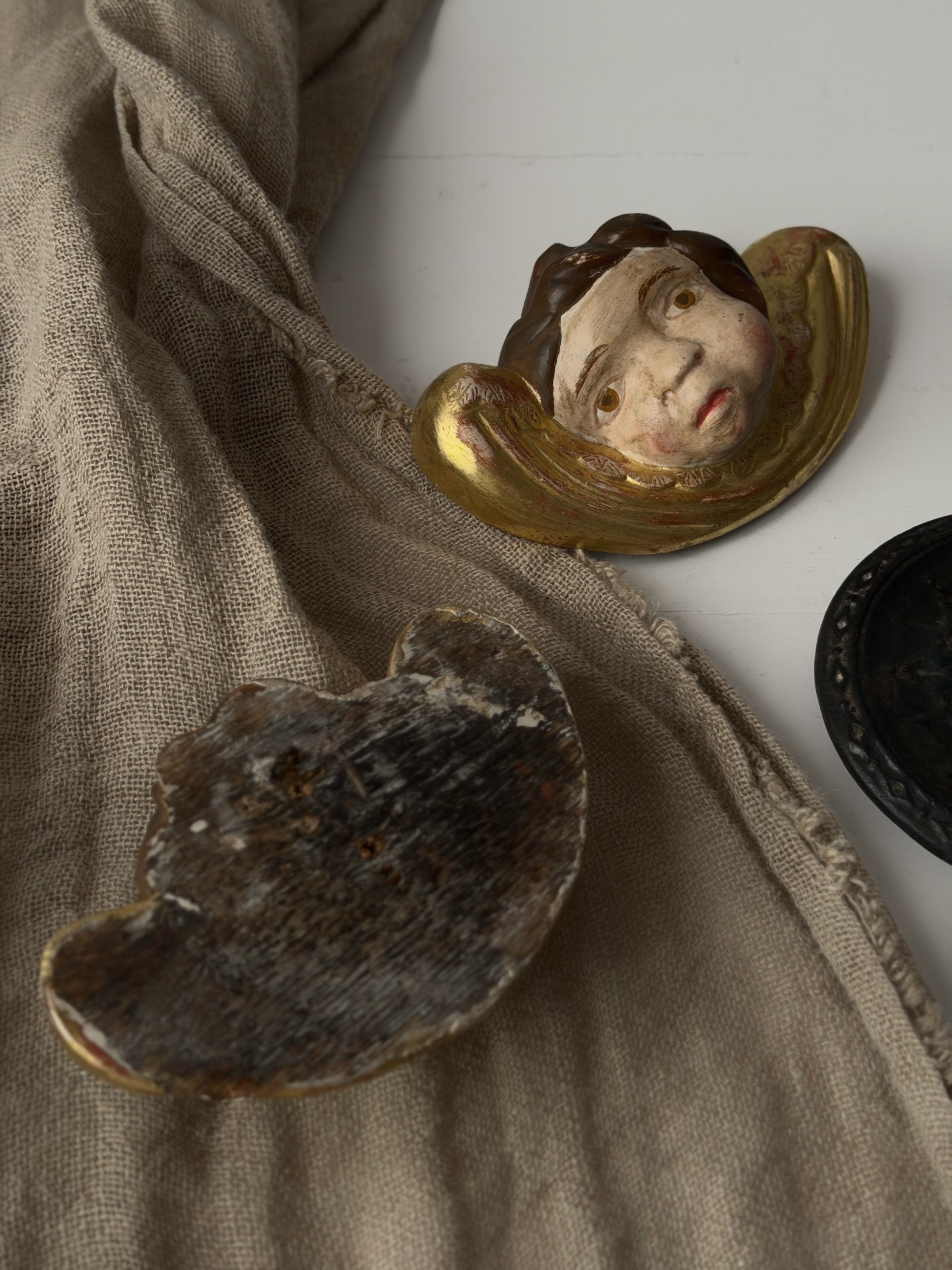 Antique wooden putti resting on natural linen showing the painted face and raw wood back